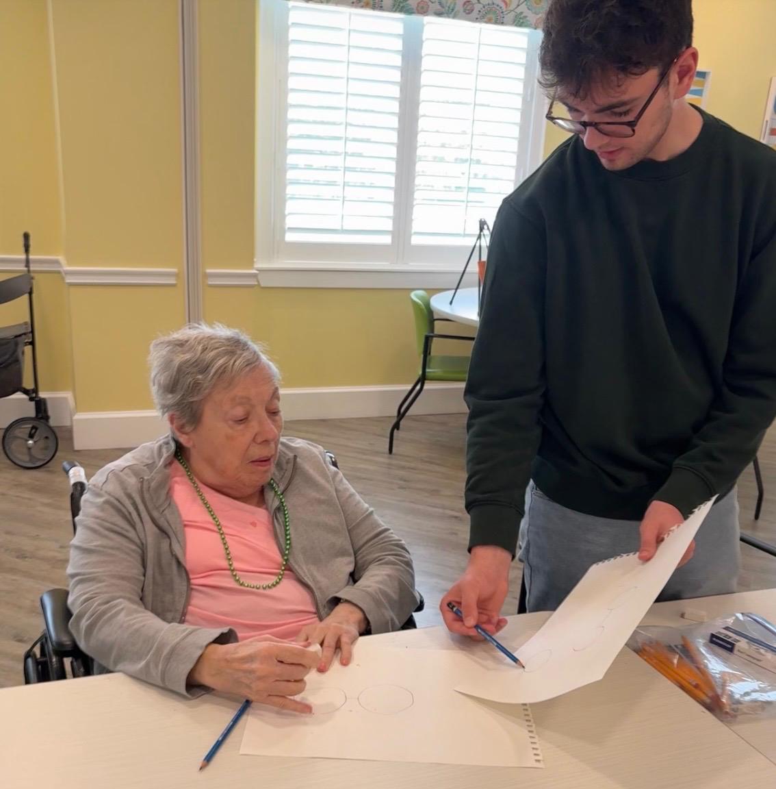 Aidan Fogel guiding a senior resident through a drawing session at an assisted living facility